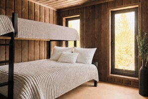 A bunk bed with a textured white bedding, wooden walls, and a large window with a view of trees.