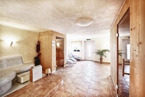 A spacious indoor area with a tiled floor, a wooden bench, a cushioned seating area, and a door leading to another room.