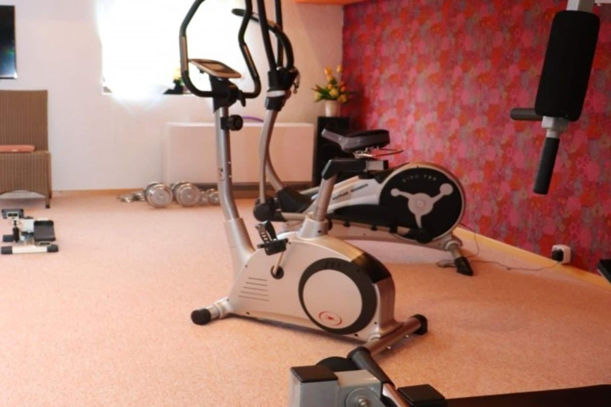 Een fitnessapparaat in een kamer met een radiator, een tafeltje met een plant, en een wand met een bloemenmotief.