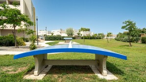Una cadira de formigó amb respatller blau en una zona verda, amb edificis al fons.
