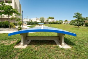 A concrete bench with a blue top in a grassy area with buildings in the background. - Charming Villa by Sérignan Beach (Sérignan)