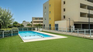 Un edifici modern amb una piscina, envoltat d'unes zones verdes i sota un cel serè.