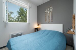 A bedroom with a bed, a bedside table with a lamp, a wall decoration, and a window. - Charming Villa by Sérignan Beach (Sérignan)