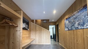 A wooden interior hallway with a tiled floor, a coat rack, and a poster on the wall. - Chalet La Centaurée - by Care Concierge (Combloux)