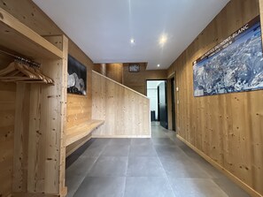 A wooden interior hallway with a tiled floor, a coat rack, and a poster on the wall. - Chalet La Centaurée - by Care Concierge (Combloux)