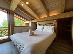 A wooden bedroom with a bed, a window, and a view of greenery. - Chalet La Centaurée - by Care Concierge (Combloux)