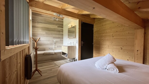 A wooden cabin interior with a bed, a bathroom with a shower, and a wooden ceiling. - Chalet La Centaurée - by Care Concierge (Combloux)