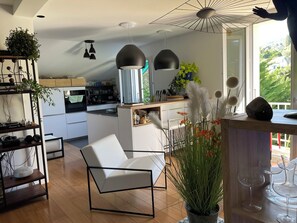 A modern kitchen with white cabinets, a central island, pendant lighting, and a view of greenery outside. - The Blue Grotto. Stay on the blue shores of Lake Geneva, in the heart of the Alps. (Évian-les-Bains)