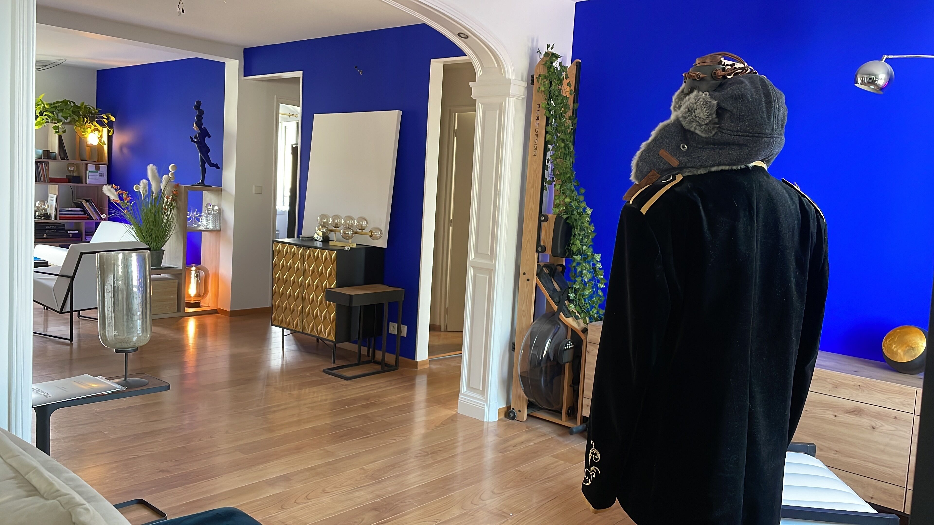 A room with a blue wall, a wooden cabinet, a mirror, and a mannequin dressed in a black robe.