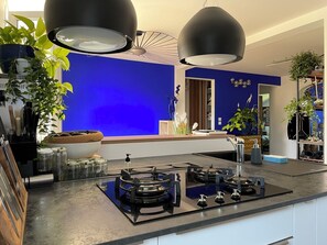 A modern kitchen with a blue accent wall, black pendant lights, and a gas stove. - The Blue Grotto. Stay on the blue shores of Lake Geneva, in the heart of the Alps. (Évian-les-Bains)