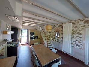 A kitchen with a wooden table and chairs, a staircase, and a stone wall. - Large family home with swimming pool (Saint-Lormel)