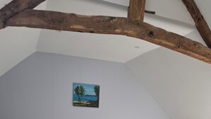 Ett sovrum med en säng, två sängbord, en tavla och synliga träbjälkar.