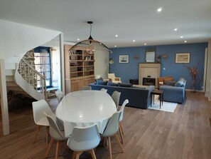 A modern living room with a dining table, chairs, a sofa, a fireplace, and a bookshelf. - Large family home with swimming pool (Saint-Lormel)