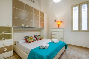 Ein Schlafzimmer mit Bett, Kleiderschrank, Ablagefläche mit Tassen, Lampe und Fenster.