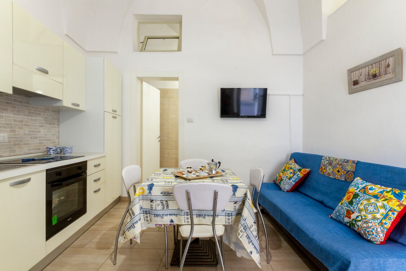 A compact kitchen with a dining table, chairs, and a blue sofa with colorful cushions.