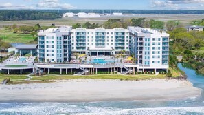 Ein mehrgeschossiges Hotel mit Poolbereich in Strandnähe und am Wasser.