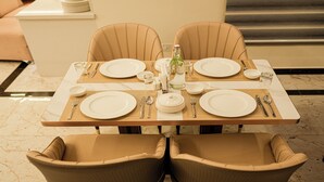 A dining table set with plates, cutlery, and a bottle, surrounded by cushioned chairs. - Tulip Inn Bengaluru Hoodi (Bengaluru)