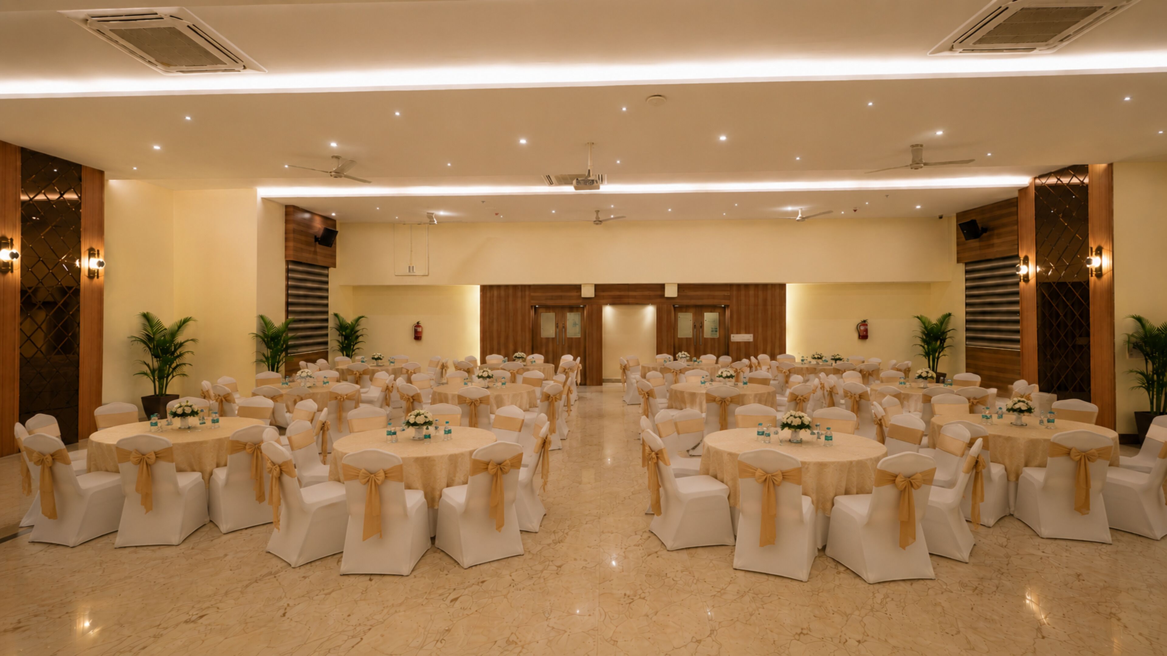 Un salón de conferencias amplio con varias mesas redondas, cada una rodeada de sillas con fundas color beige.