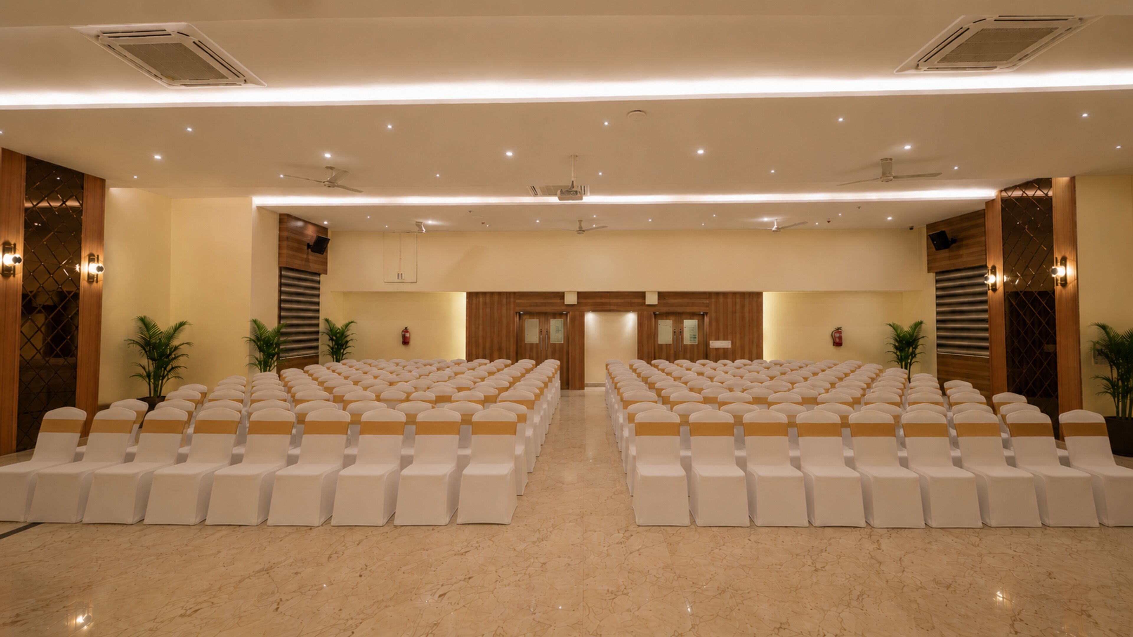 A conference room with rows of chairs, a stage, and a ceiling with recessed lighting.