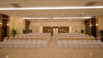 A conference room with rows of chairs, a stage, and a ceiling with recessed lighting.