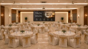 A conference room with round tables, chairs with gold sashes, and a large screen displaying hotel amenities. - Tulip Inn Bengaluru Hoodi (Bengaluru)