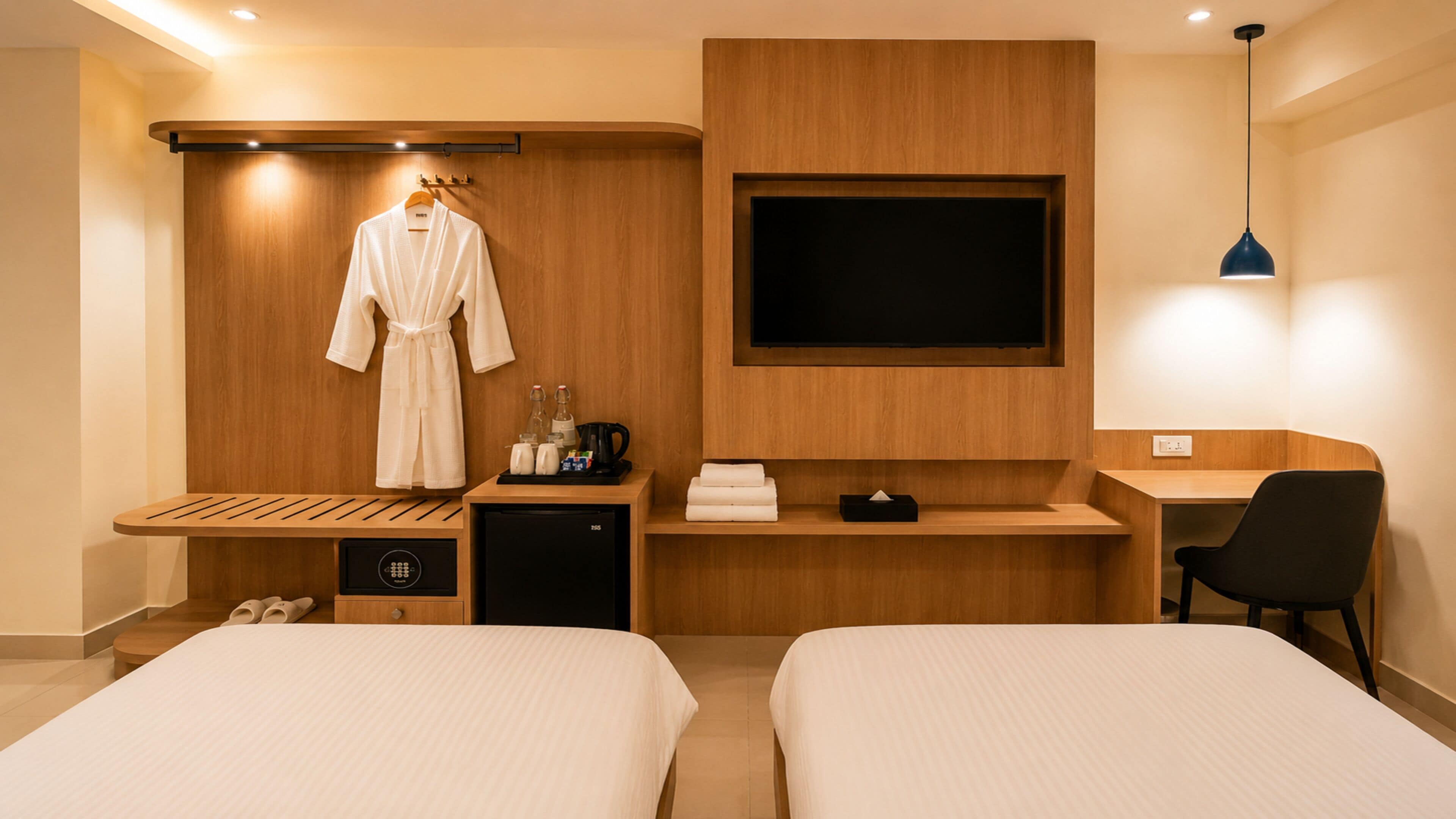 A hotel room with two beds, a desk, a TV, a robe, and a coffee maker.