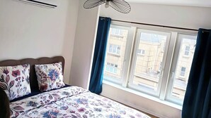 Un dormitorio con cama, aire acondicionado, ventilador de techo y ventana con cortinas.