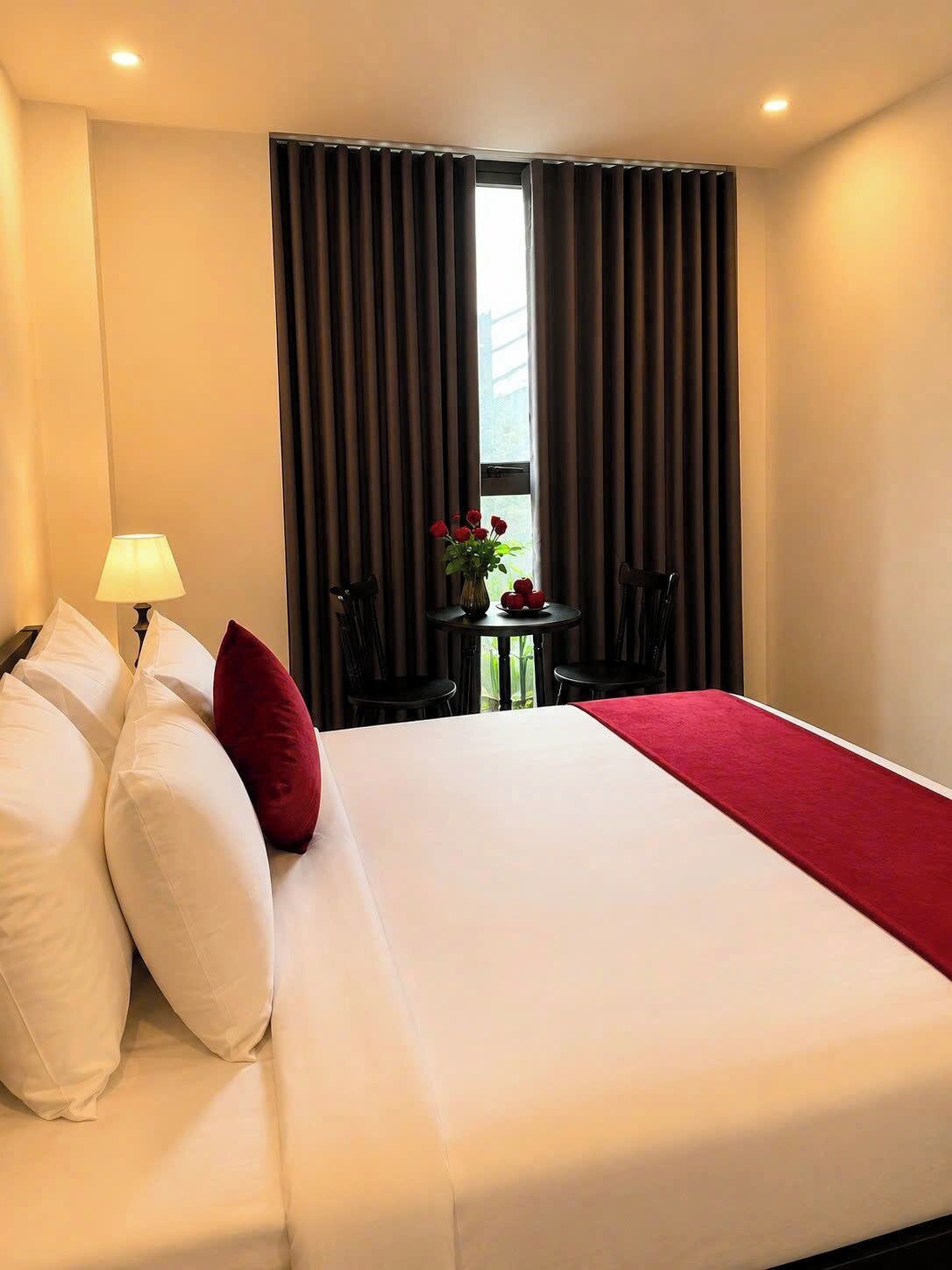 A hotel room with a bed, a table with a vase of flowers, and a window with curtains.