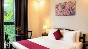 Habitación de hotel con una cama grande, una mesita de noche, una lámpara, una silla, una ventana con cortinas y un cuadro en la pared.