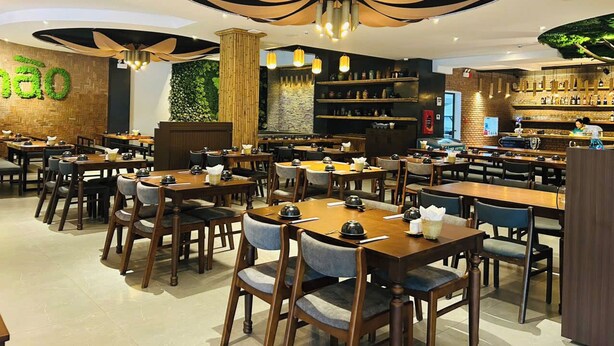 Un restaurante con varias mesas y sillas, una zona de bar y una pared decorada con plantas.
