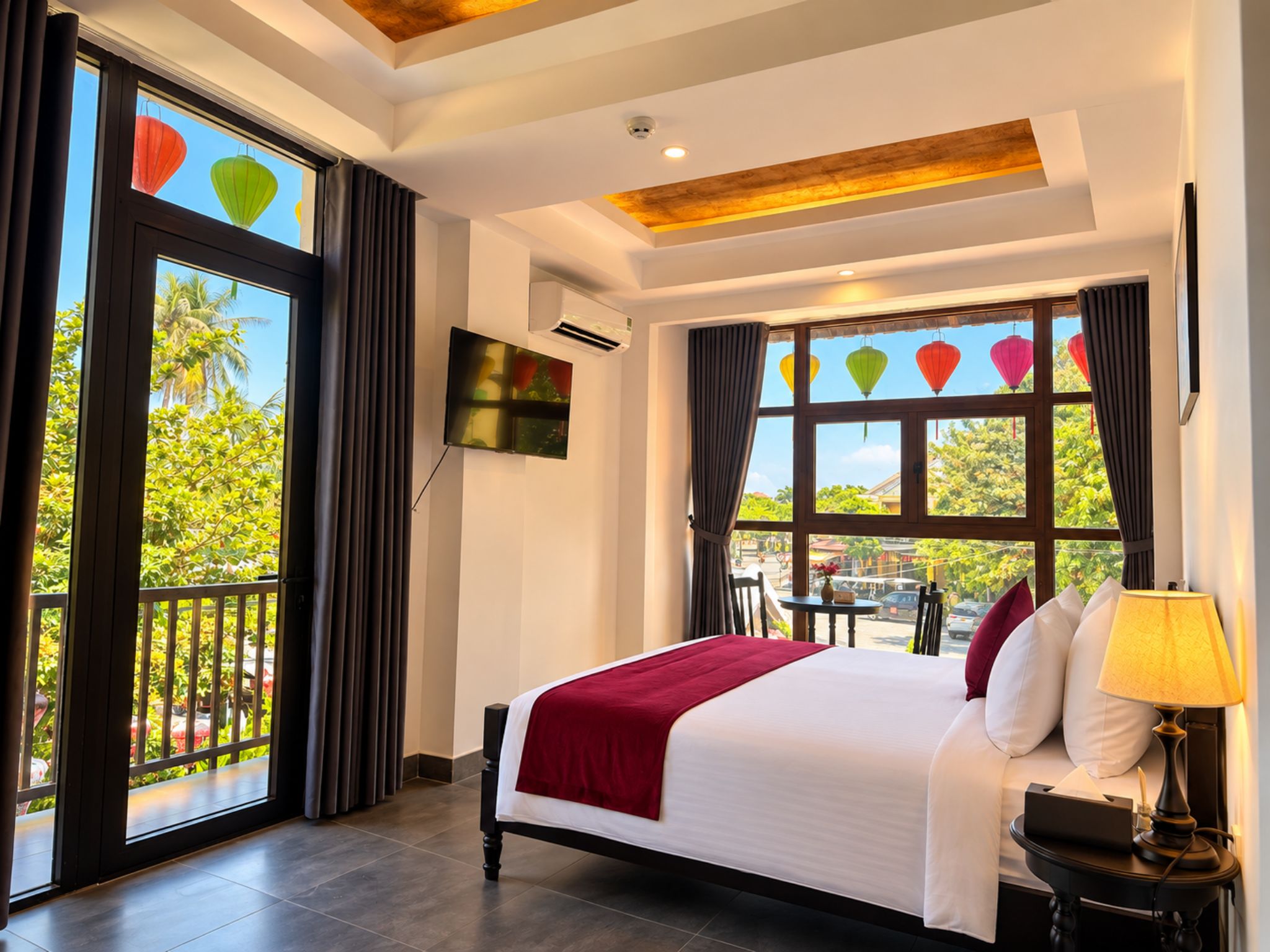 Quarto de hotel com uma cama grande, televisão fixada na parede e varanda com cortinas.