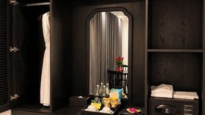 Habitación de hotel con armario empotrado, espejo, minibar, refrigerador pequeño y un cesto de basura.