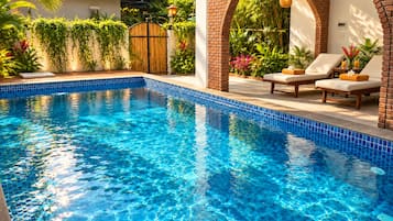 Una piscina azul cristalina con bordes de azulejos, rodeada por un muro de ladrillo y una cerca de madera.