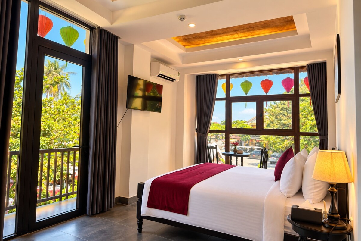 A hotel room with a large bed, a TV mounted on the wall, and a balcony with curtains.
