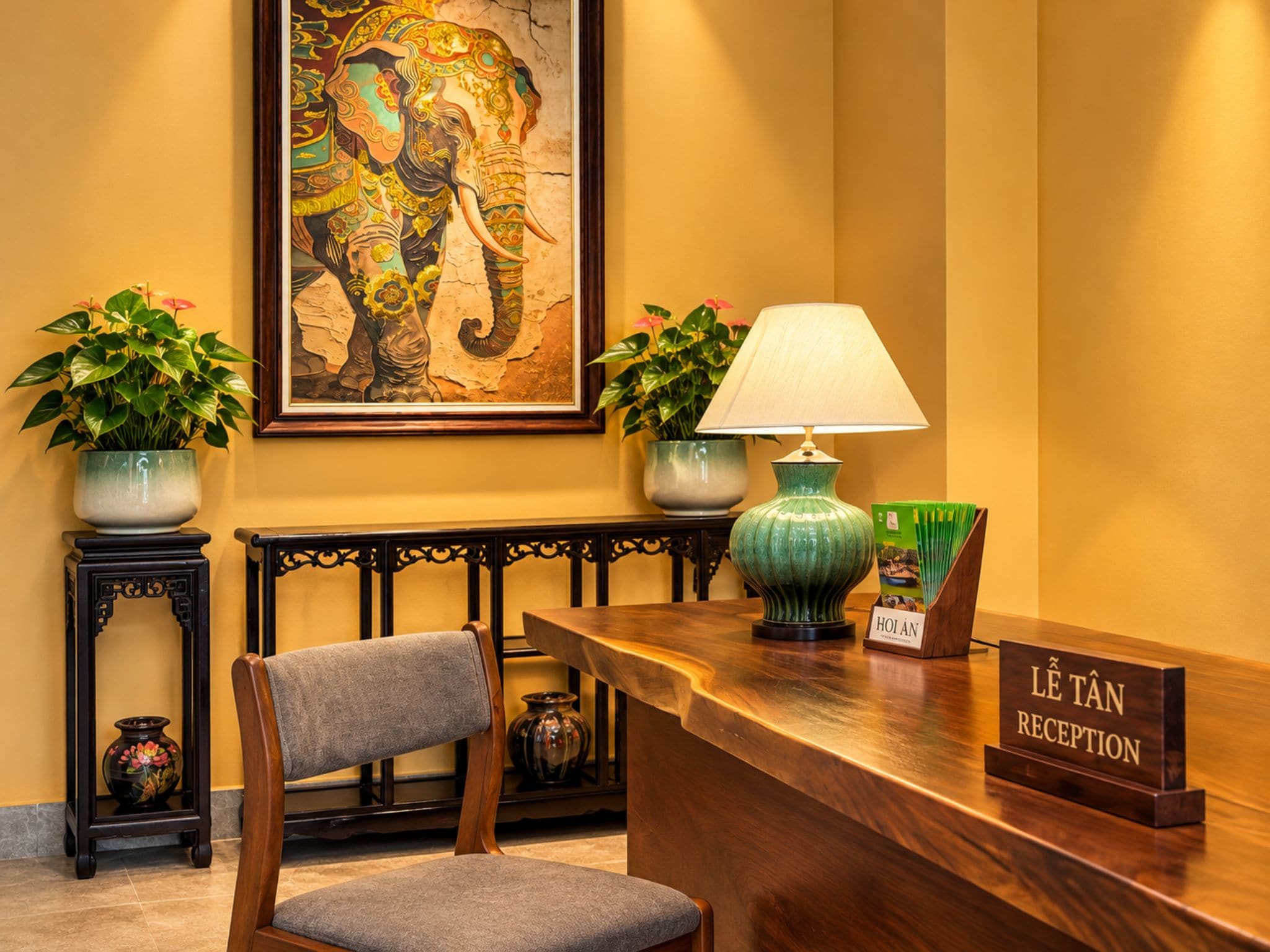 A reception desk with a chair, a lamp, two potted plants, and a framed artwork on the wall.