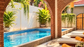 Una piscina con borde de azulejos, rodeada de arcos de ladrillo, plantas en macetas y sillas de descanso con toallas.