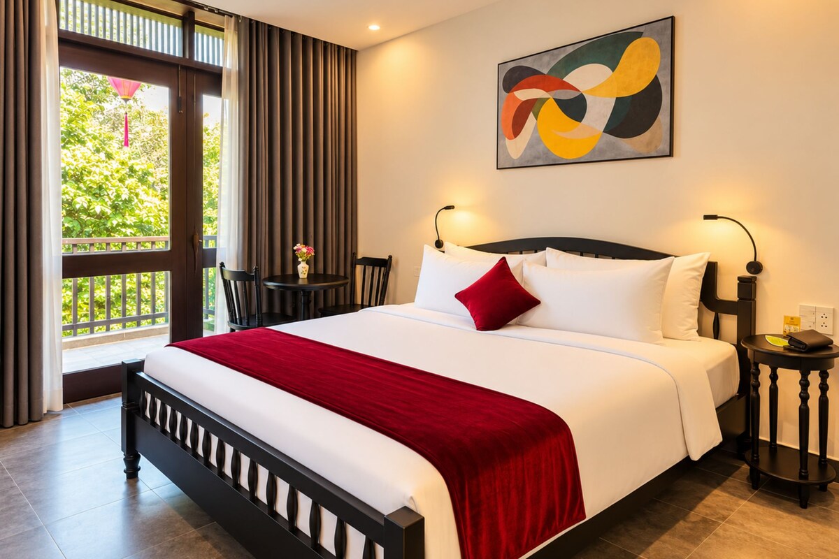 Quarto de hotel com cama, mesa de cabeceira, uma cadeira, janela com cortinas e um quadro na parede.