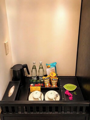 A minibar with a kettle, bottles, snacks, and a small flower. - Happy Life Heritage Hoi An Hotel (Da Nang)