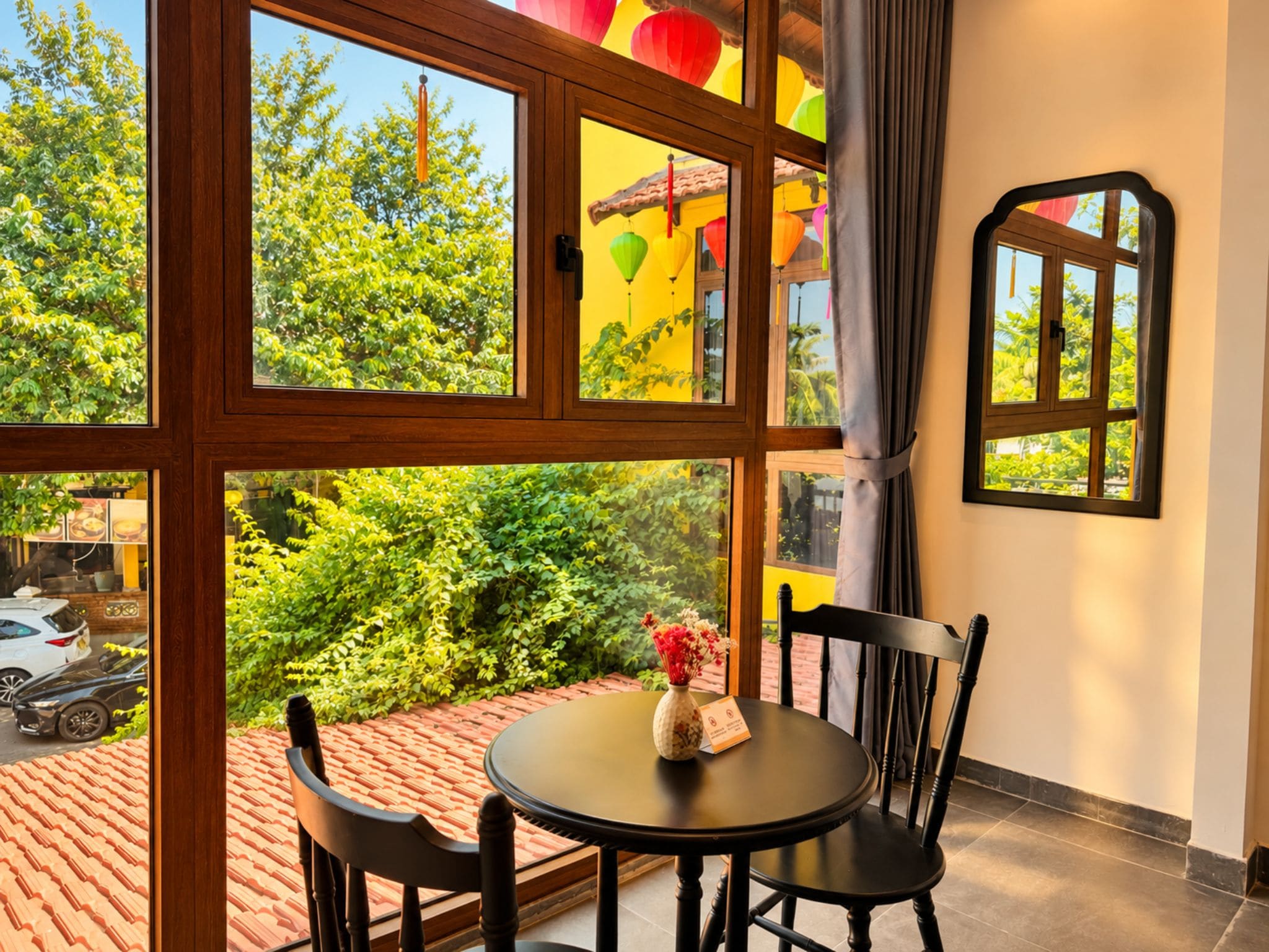 A room with a large window, a round table with chairs, and a vase with flowers.