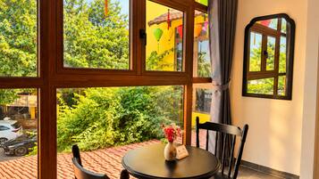 A room with a large window, a round table with chairs, and a vase with flowers.