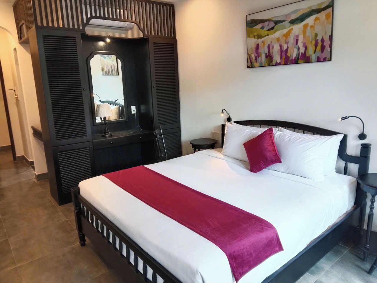 A hotel room with a bed, a nightstand, a lamp, a mirror, and a wardrobe.
