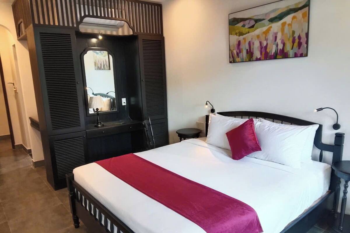 Ein Hotelzimmer mit Bett, Nachttisch, Lampe, Spiegel und Kleiderschrank.