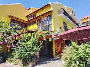 A yellow building with a balcony, potted plants, and outdoor seating. - Happy Life Heritage Hoi An Hotel (Minh An)