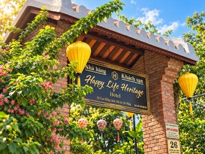 A sign for Happy Life Heritage Hotel with a brick facade and hanging lanterns. - Happy Life Heritage Hoi An Hotel (Da Nang)