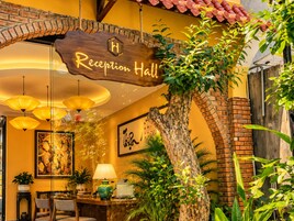 Uma área de recepção com uma placa de madeira que diz 'Reception Hall', uma árvore grande e uma mesa com cadeiras.