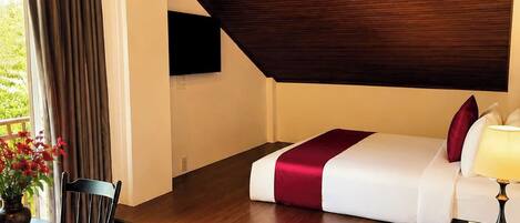 Habitación de hotel con techo de madera, cama con colcha roja y blanca, mesita de noche con lámpara, una silla y una mesa con un jarrón de flores.