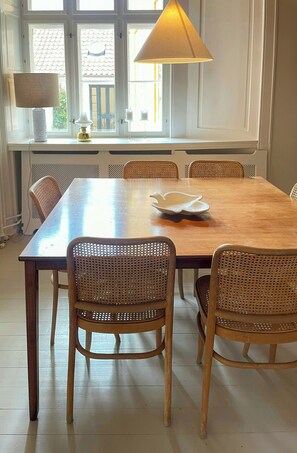 Ein Essbereich mit Holztisch, Korbstühle, einem weißen Kerzenhalter und einer Lampe.