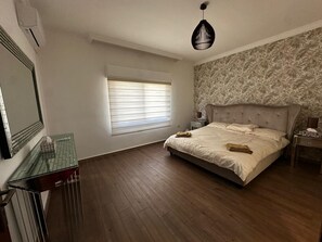 Ein Schlafzimmer mit einem großen Bett, einem Nachttisch, einem Spiegel und einem Fenster mit Jalousien.