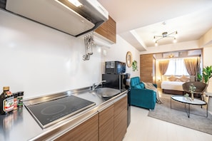 A modern kitchen with a built-in stove, a sink, and a microwave. There is a dining area with a teal sofa and a small table. The room has wooden cabinets and a ceiling light fixture.