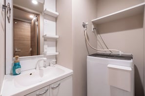 A bathroom with a sink, mirror, towel rack, and a shower unit.